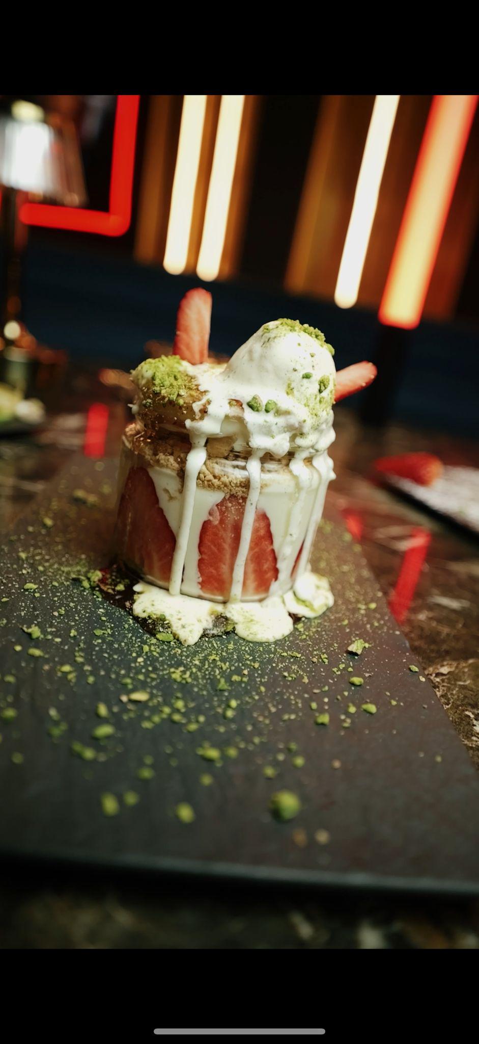 Ein Dessert auf Teller mit Eis, Erdbeeren, Pistazien und rotem Kuchen im edlen Dekor.