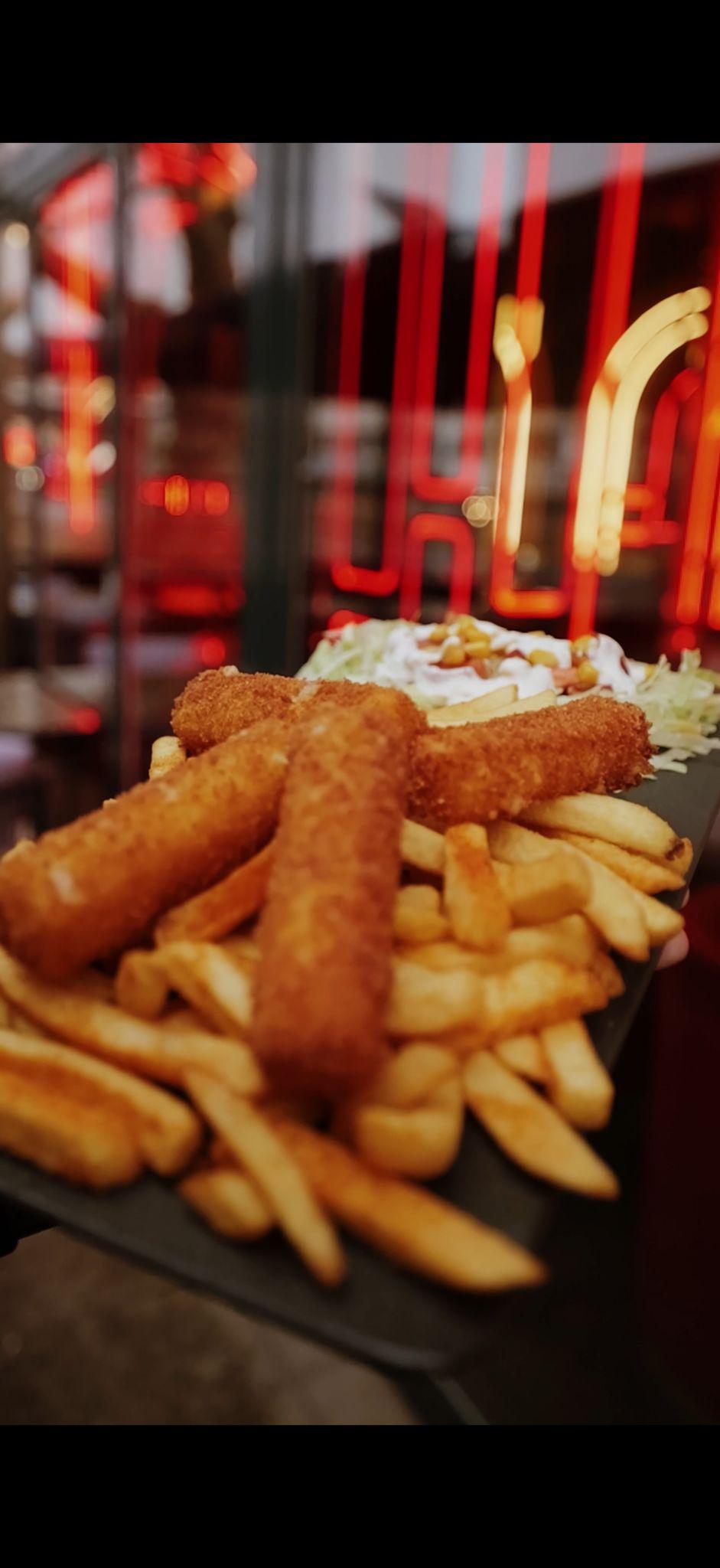 Ein Teller mit Pommes, Fischstäbchen und Salat, im Hintergrund rote Neonlichter.